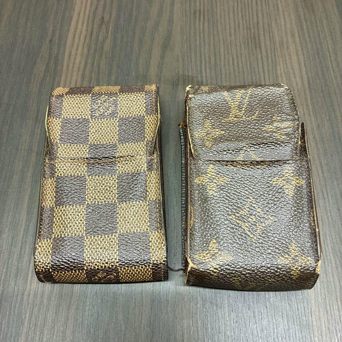 Two Louis Vuitton cigarette cases in Damier and Monogram canvas placed side by side on a wood surface.