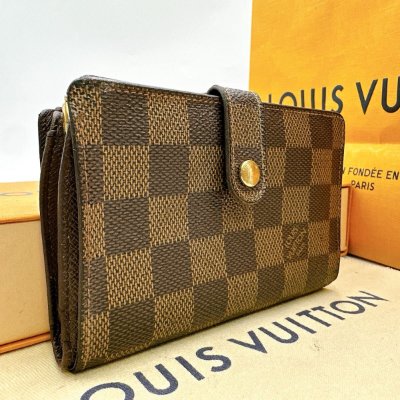 Brown Louis Vuitton Damier-pattern bi-fold wallet with snap tab displayed on branded boxes.
