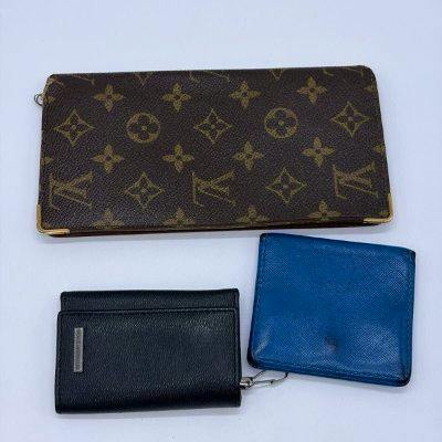 Three leather wallets/key cases on a white background: a Louis Vuitton monogram long wallet, a black leather wallet, and a blue leather wallet.