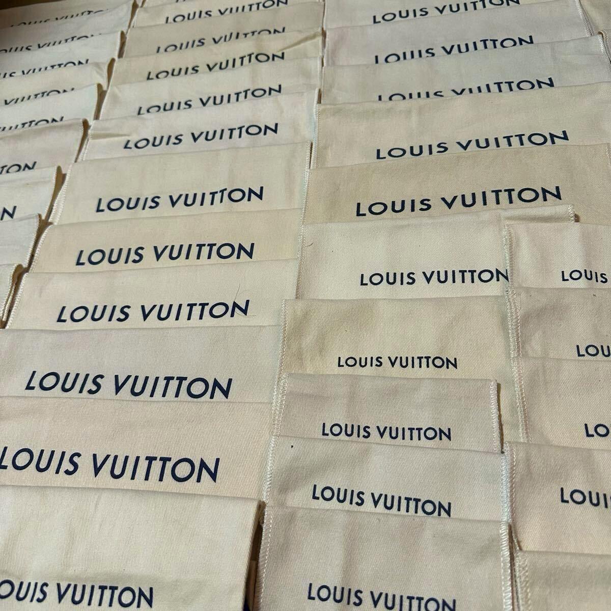 Close-up of multiple cream-colored Louis Vuitton dust bags with the navy LOUIS VUITTON logo printed on them.