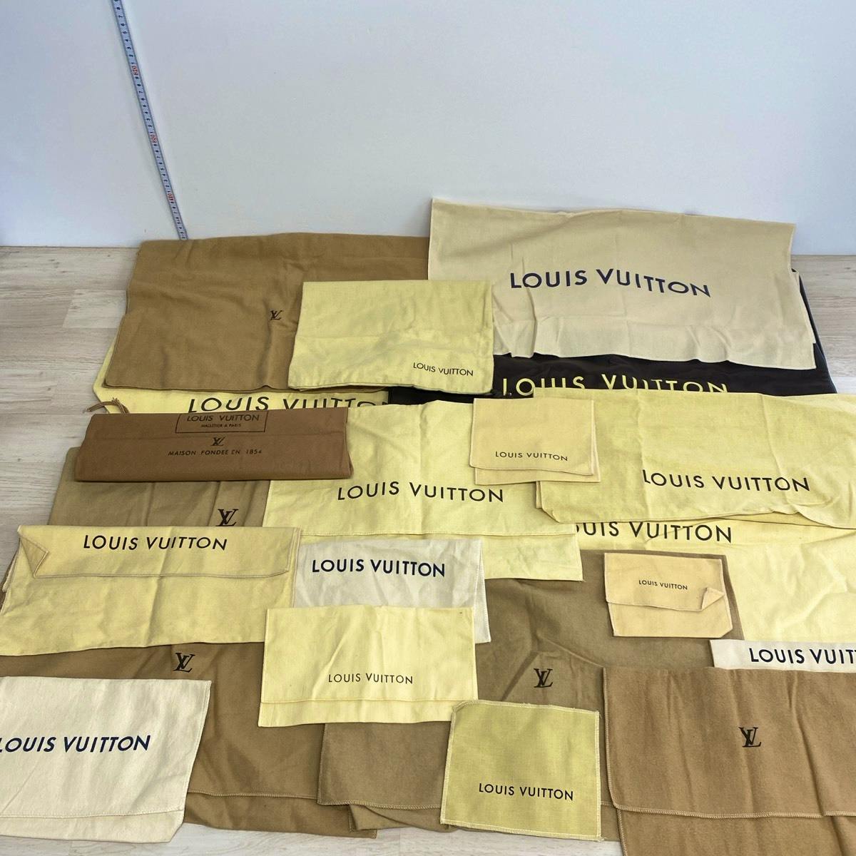 Multiple beige and brown Louis Vuitton cotton dust bags and pouches arranged flat on a floor.