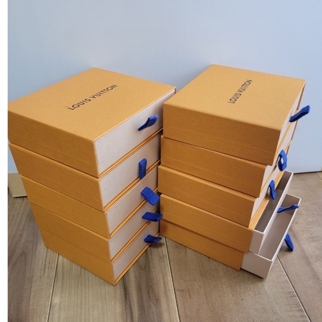 Ten orange Louis Vuitton paper boxes with blue pull ribbons stacked together, with some drawer-style boxes partially open.
