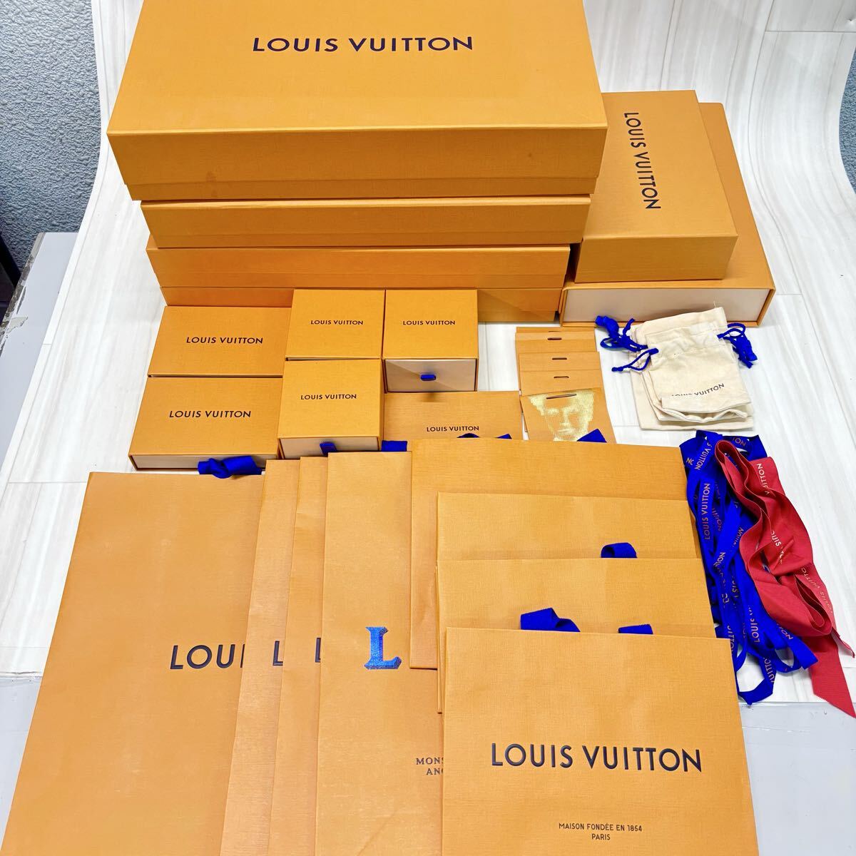 Multiple Louis Vuitton orange storage boxes, shopping bags, ribbons, and small dust bags arranged on a table.