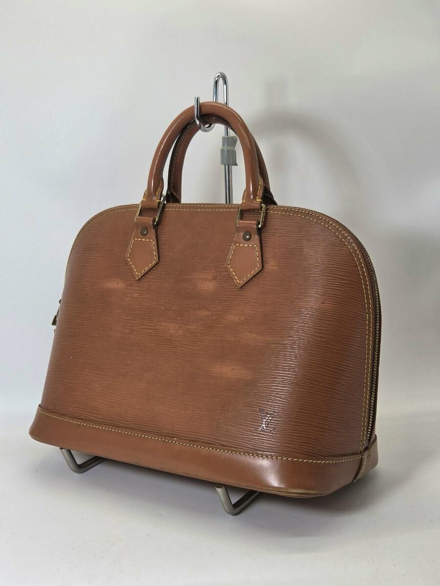 Brown Louis Vuitton Épi Alma handbag photographed front-on resting on a stand.