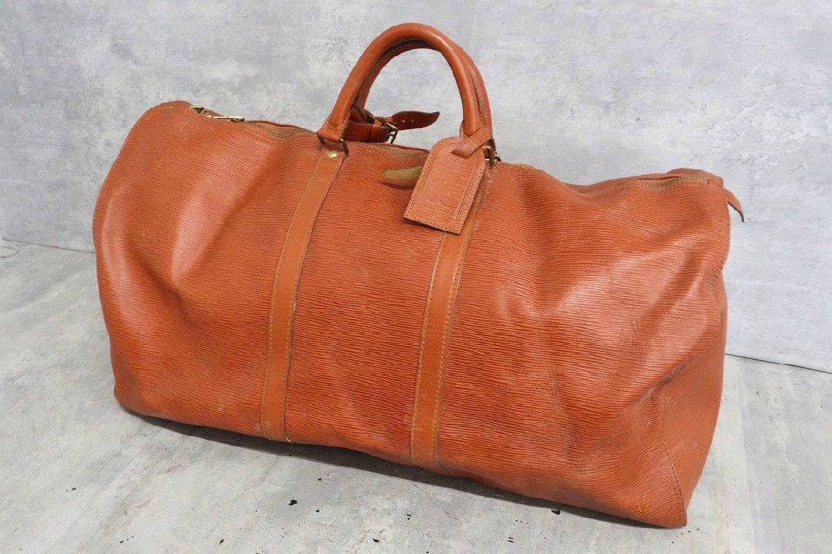 Camel-colored Louis Vuitton Epi Keepall 60 leather travel bag on a gray background.