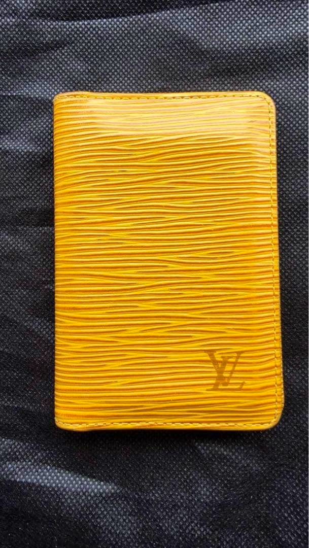 Closed LOUIS VUITTON Epi card case in yellow cow leather with visible LV logo on a black background.