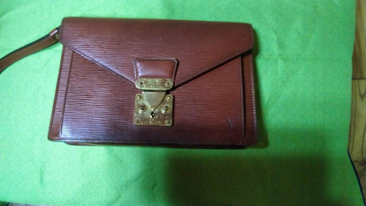 Brown Louis Vuitton Epi leather clutch bag with wrist strap and gold-tone clasp shown on a green background.