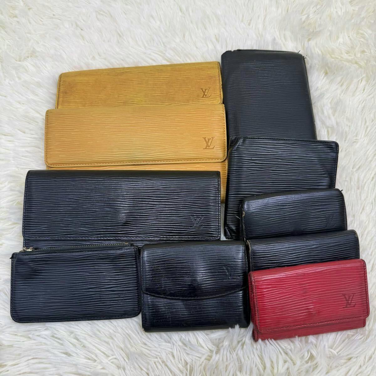 Multiple Louis Vuitton Epi leather wallets and small cases in black, red, and yellow laid out on a white surface.