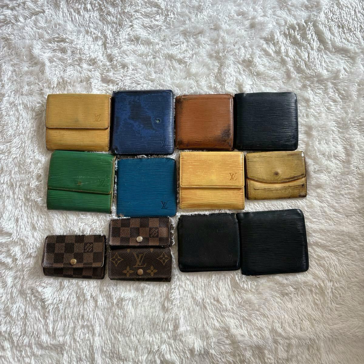 Thirteen Louis Vuitton cow leather wallets and key cases in various colors and patterns arranged on a white furry background.