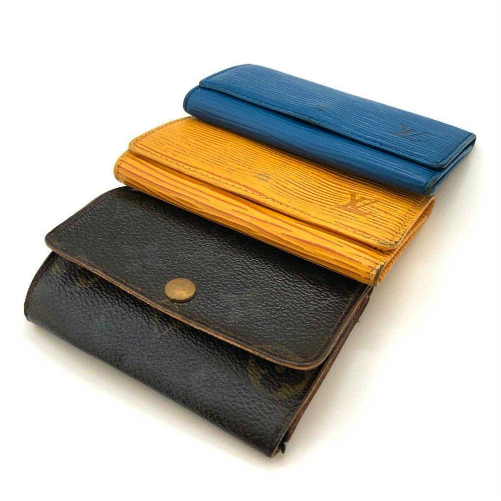 Three Louis Vuitton key cases/wallets — blue, yellow, and dark brown — stacked and photographed on a white background.