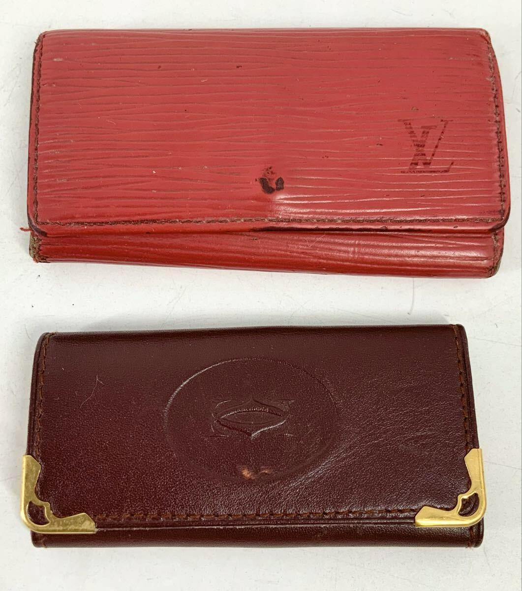 Two leather key holders on a white background: a red textured Louis Vuitton Epi key holder on top and a burgundy leather key holder with gold corner protectors below.