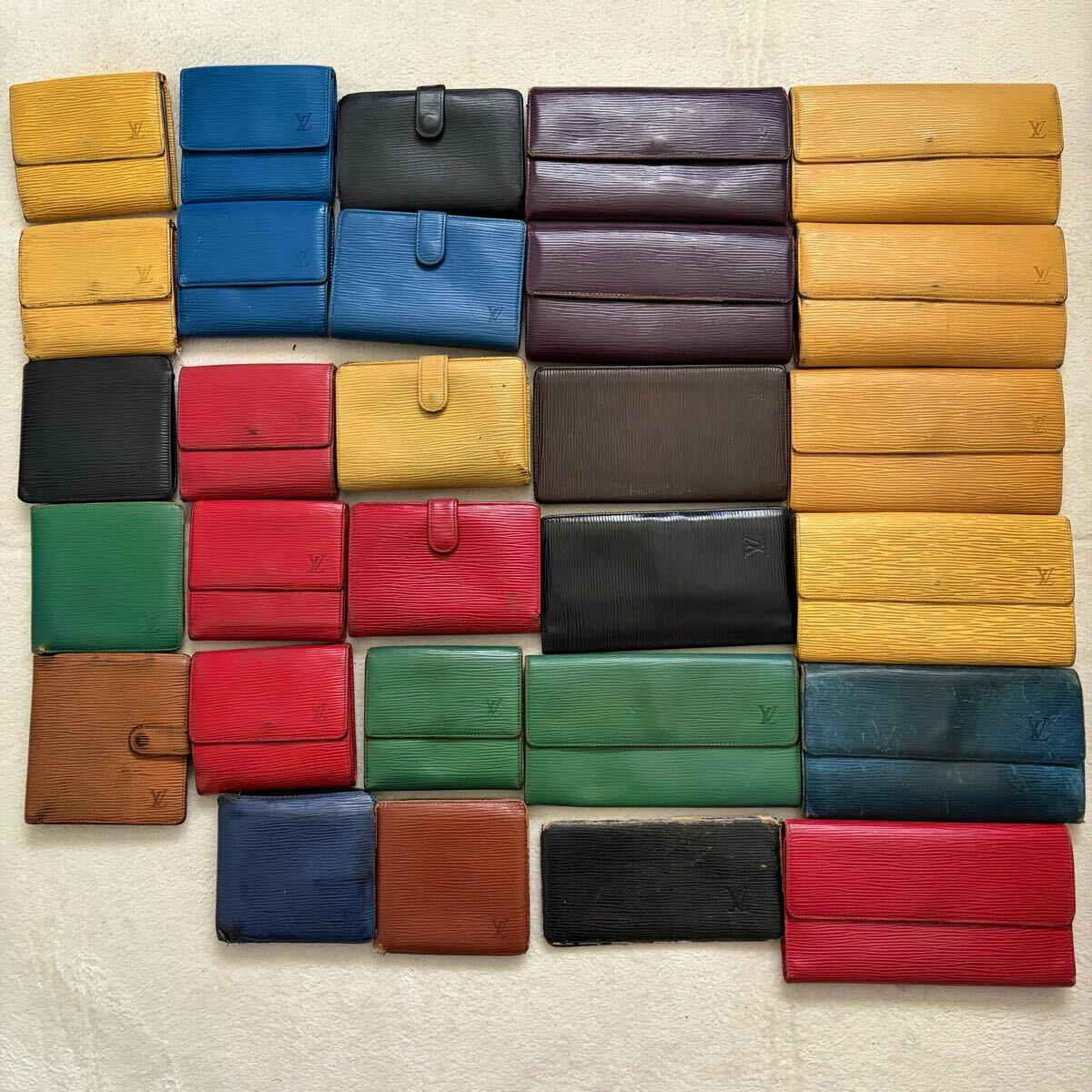 Multiple Louis Vuitton wallets and small leather cases in various colors arranged in a grid on a light surface.