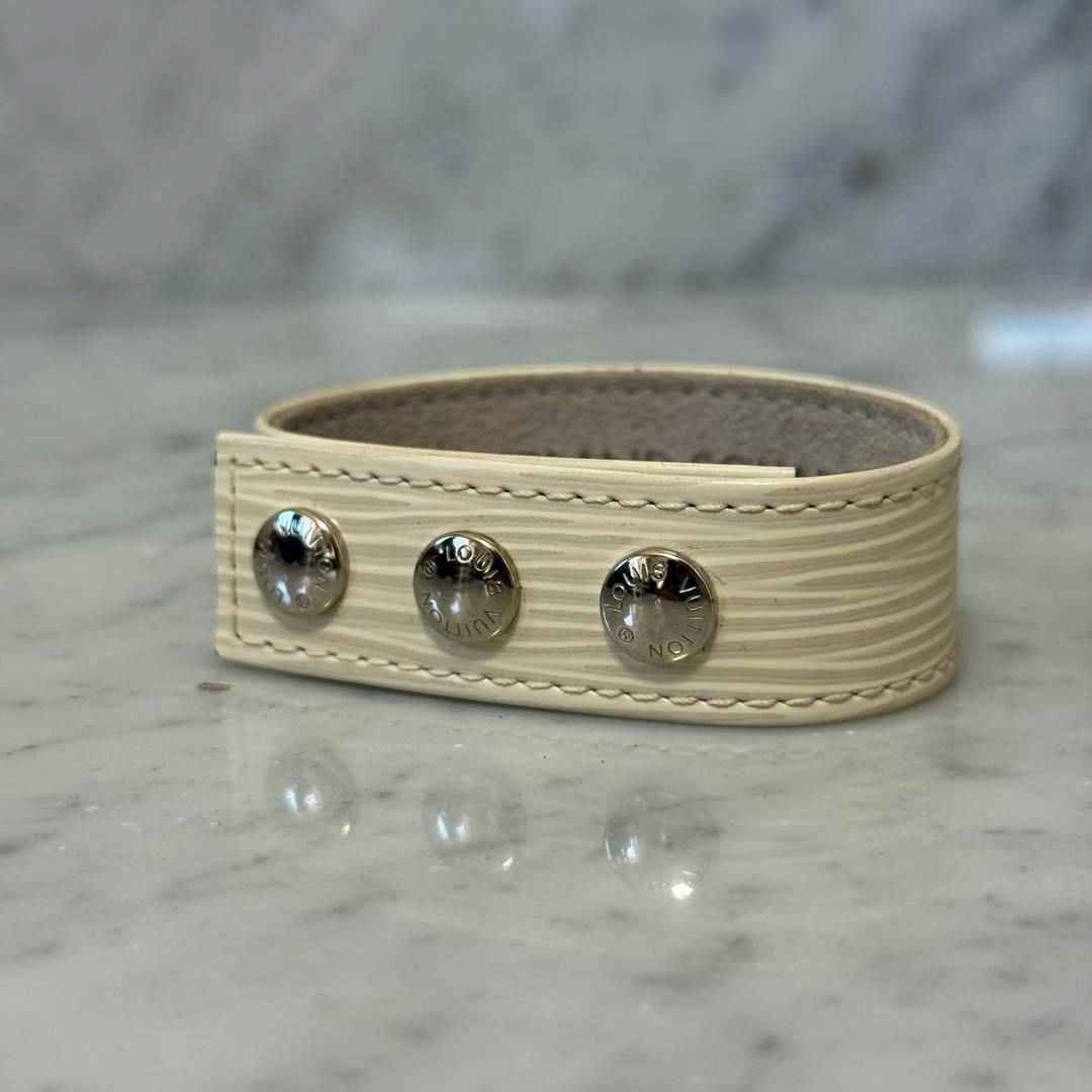 White Epi cow leather Louis Vuitton bracelet with three metal studs on a marble surface.