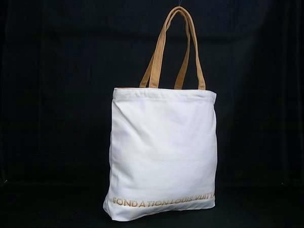White canvas Louis Vuitton Fondation tote bag with beige shoulder straps photographed against a black background.