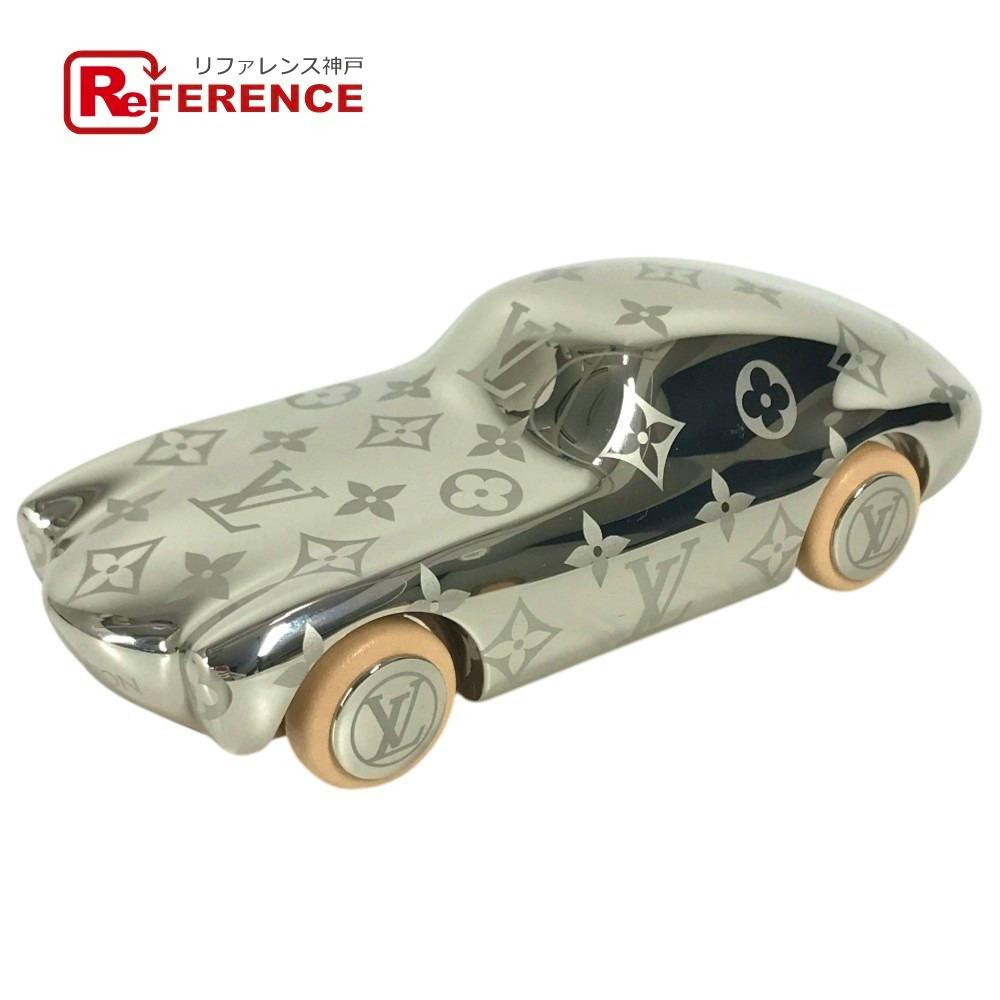 Silver Louis Vuitton monogram metal car objet with tan/gold wheels shown on a white background.