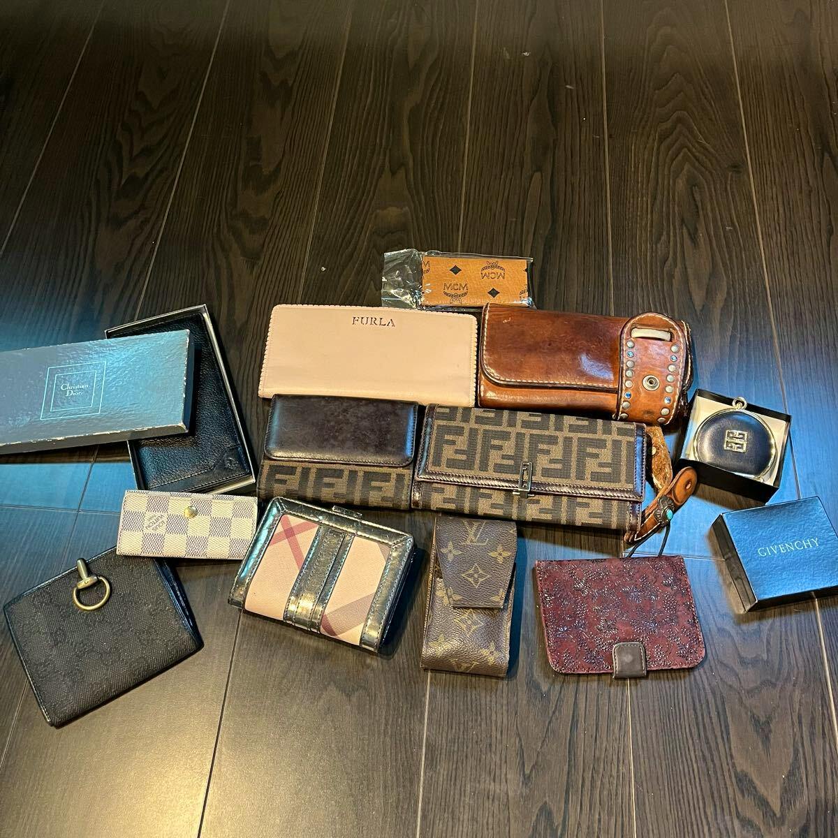 A collection of assorted wallets, key cases, and small leather accessories from multiple brands arranged on a dark wood floor.