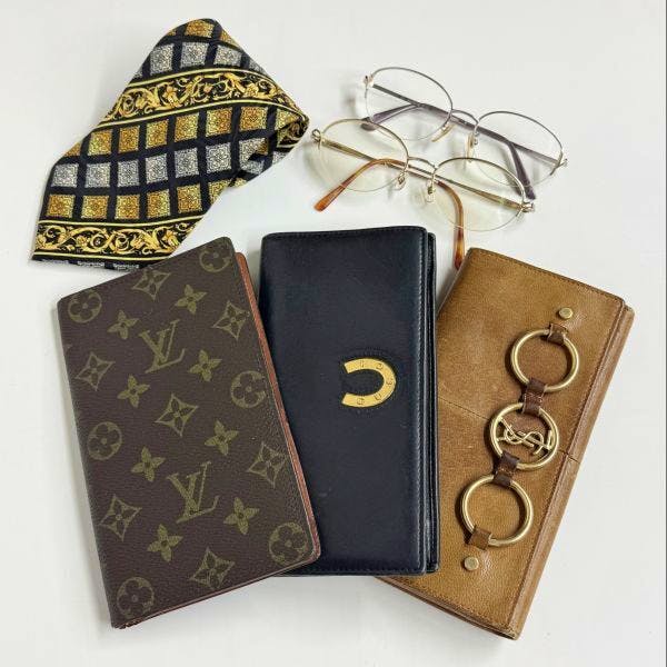 Assorted branded long wallets, eyeglasses, and a patterned tie arranged on a white surface.