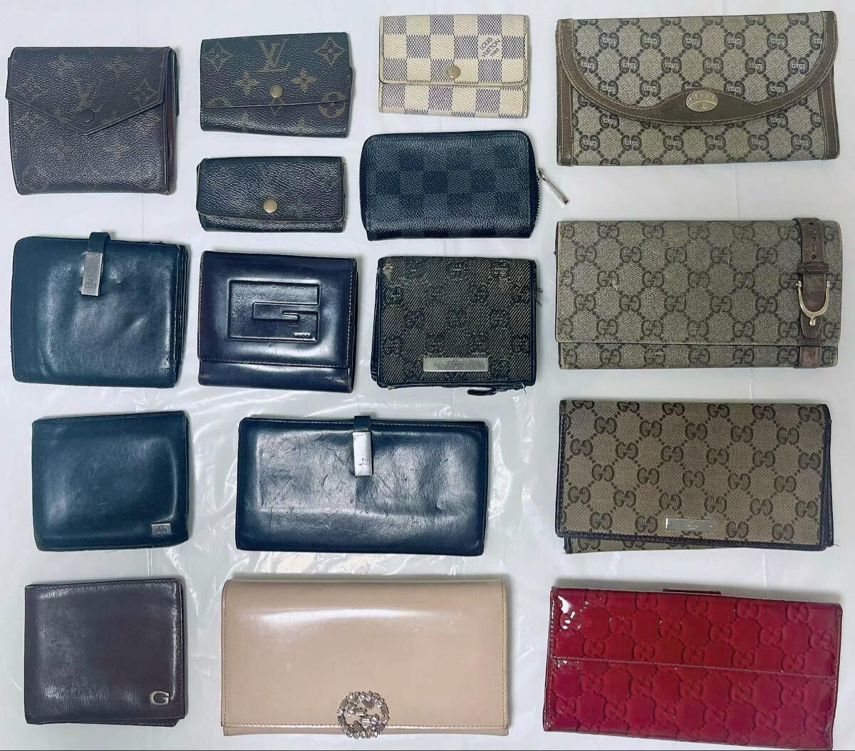 Top-down photo of assorted branded wallets and key cases (LOUIS VUITTON and GUCCI) arranged on a white surface.