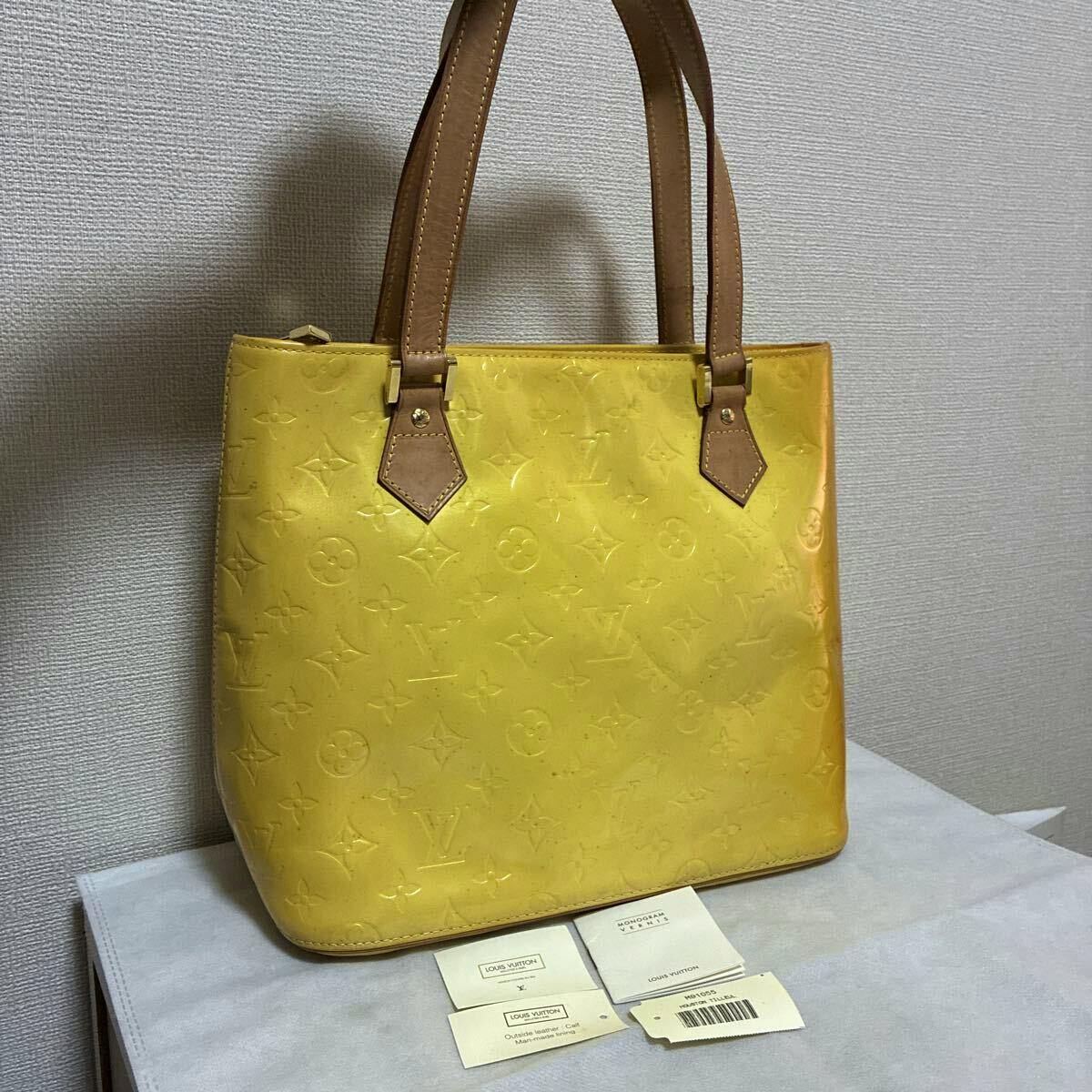 Yellow LOUIS VUITTON Vernis monogram tote handbag with brown leather handles shown upright on a surface with tags in front.