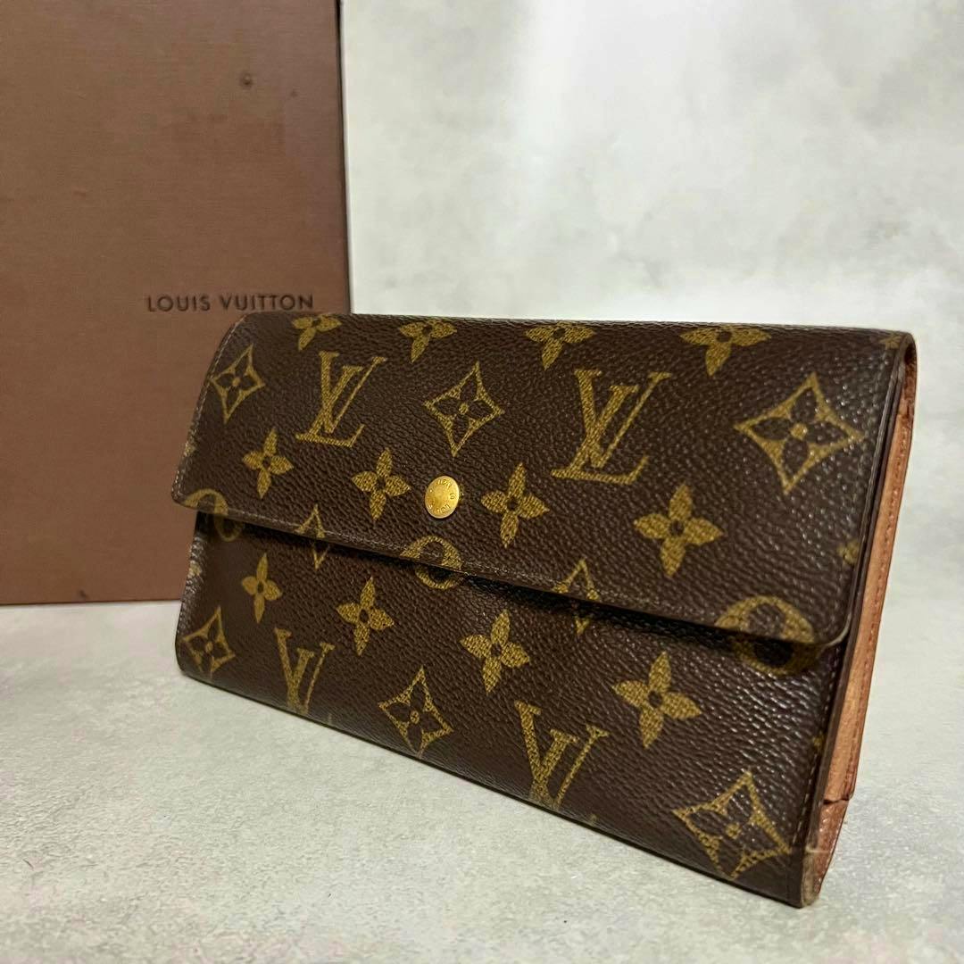 A Louis Vuitton monogram folding wallet angled on a surface with a Louis Vuitton box behind it.