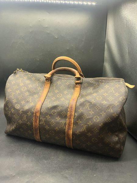 Brown Louis Vuitton monogram travel/boston bag with leather handles and trim pictured on a dark background.