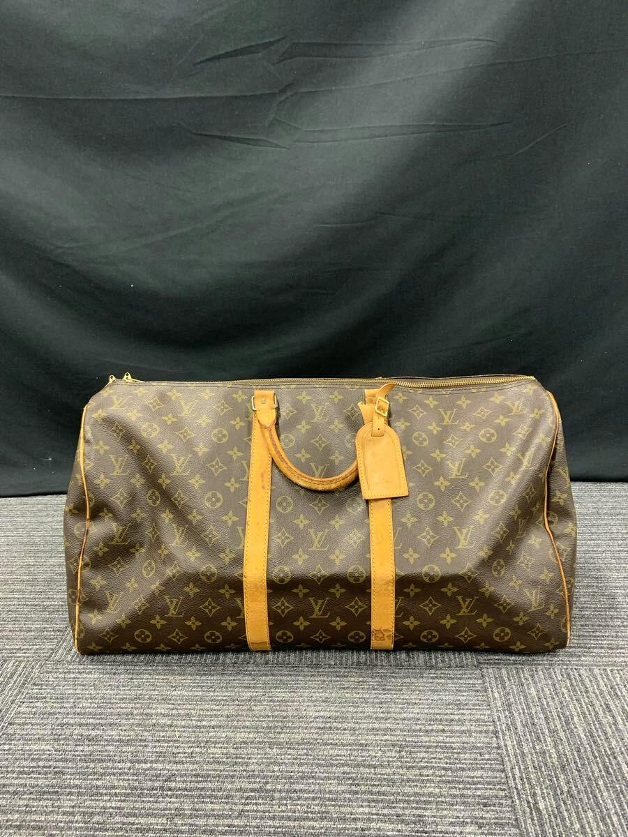 Front view of the Louis Vuitton Monogram Keepall 55 travel bag with leather handles and luggage tag on a dark fabric background.