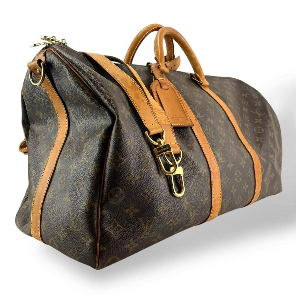 Louis Vuitton monogram canvas duffel bag with vachetta leather trim, top handles, and attached shoulder strap shown at an angle.