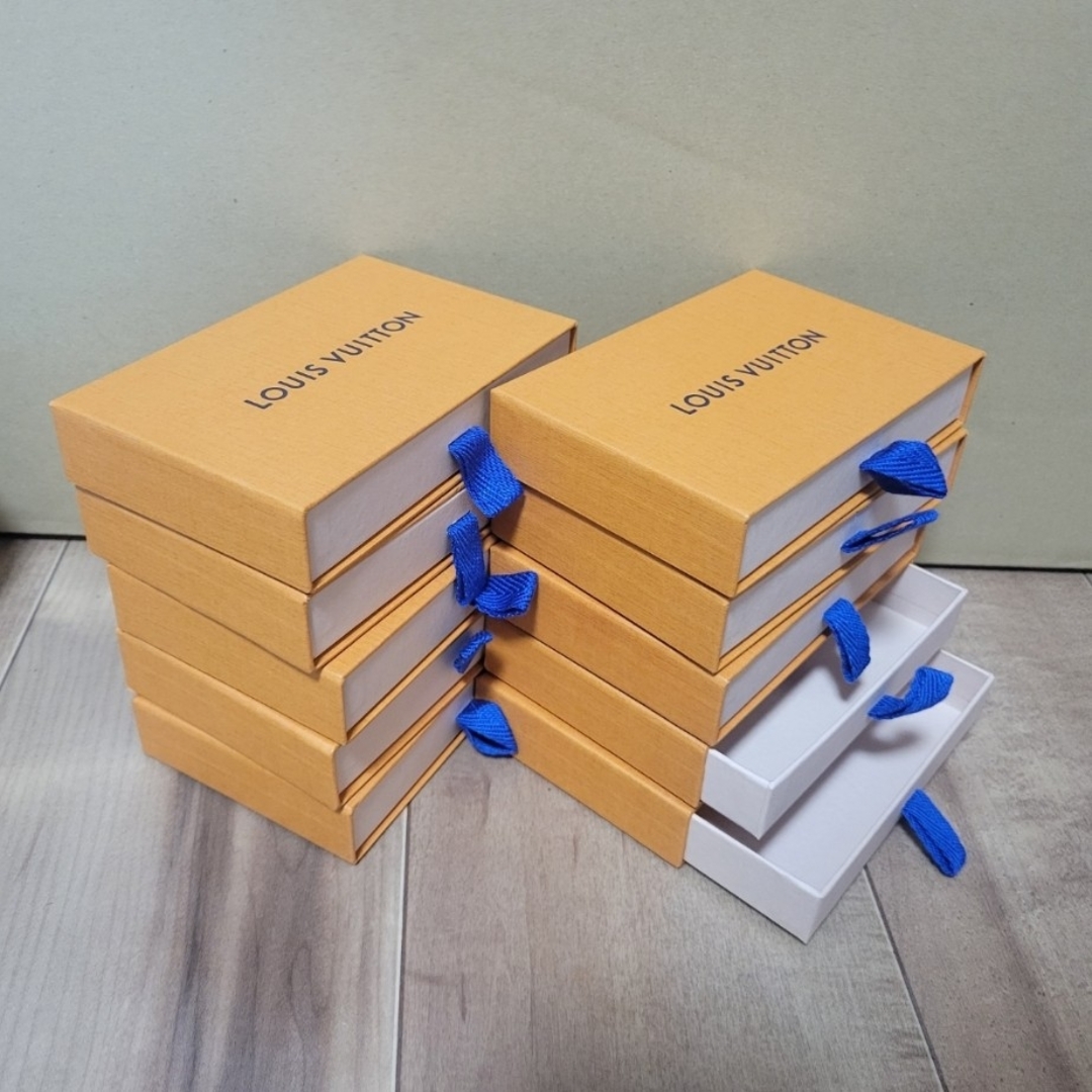 Several small Louis Vuitton orange paper boxes with blue ribbon pulls stacked on a wooden surface.
