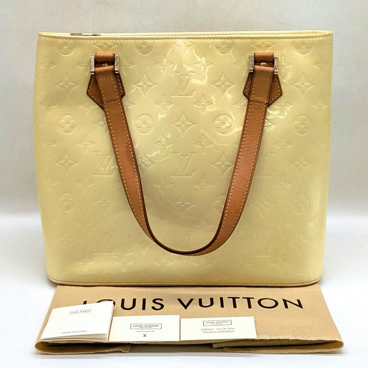 Front view of a beige Louis Vuitton Vernis tote bag with tan leather handles, shown with a Louis Vuitton dust bag and paperwork underneath.