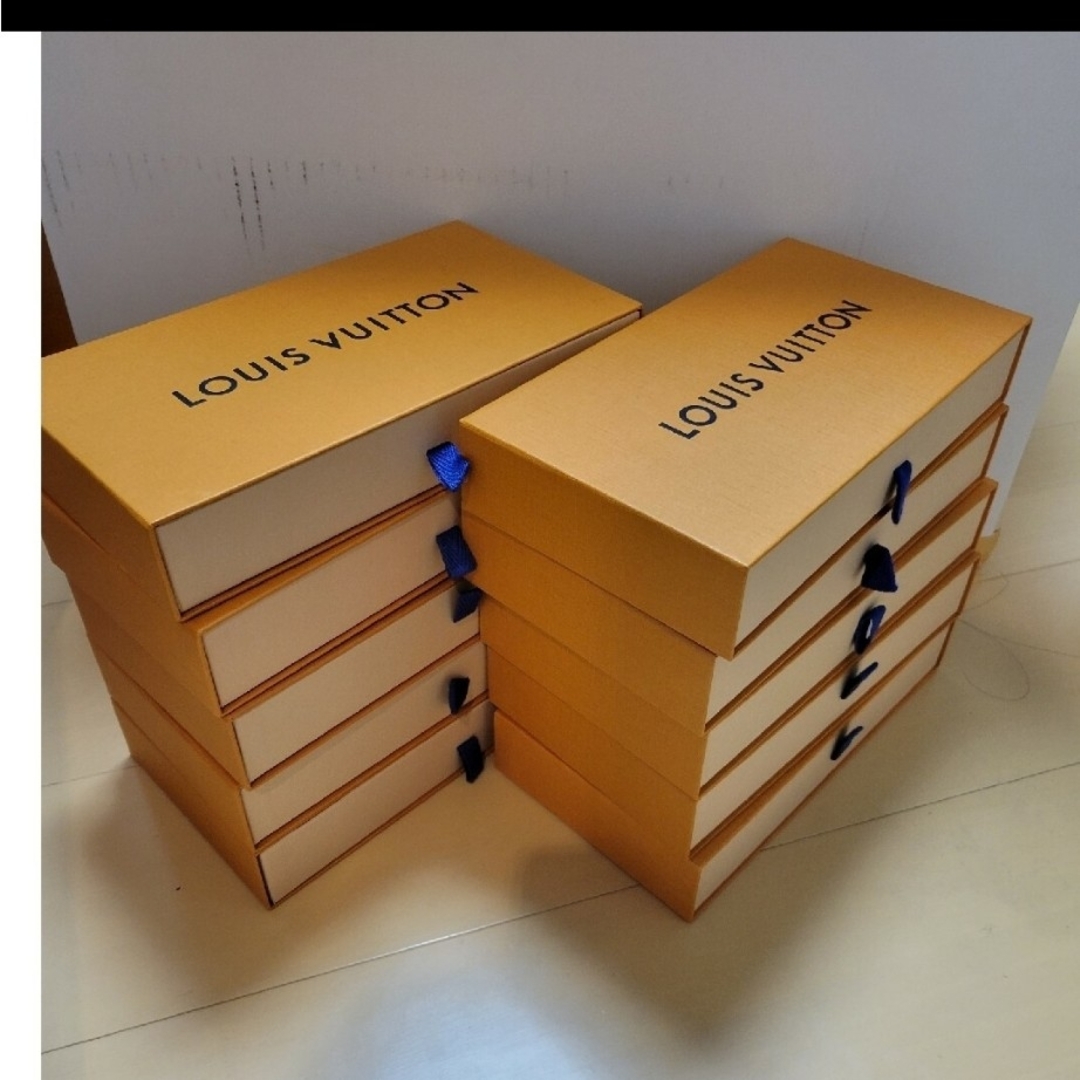 Ten Louis Vuitton long-wallet boxes (24.5 cm width) stacked in two columns on a floor, each with a blue pull ribbon.