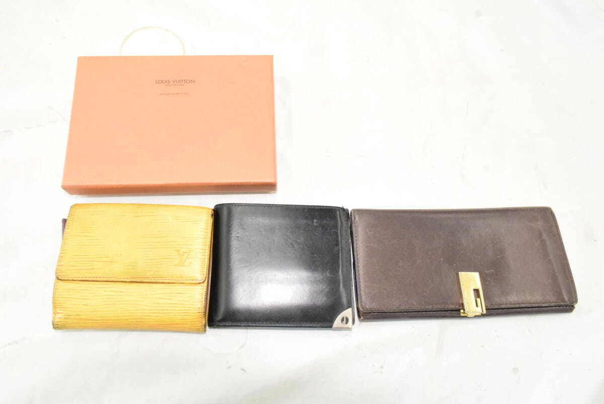 Three wallets (yellow, black, brown) and an orange Louis Vuitton box arranged side by side on a white surface.