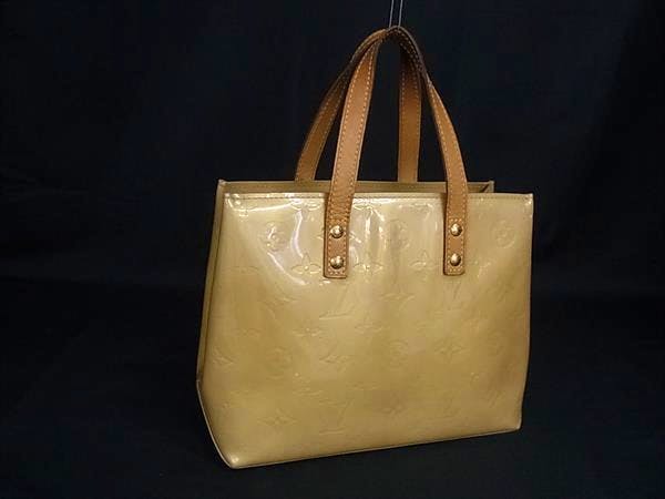 Beige Louis Vuitton Monogram Vernis Lead PM tote handbag with two leather top handles against a black background.