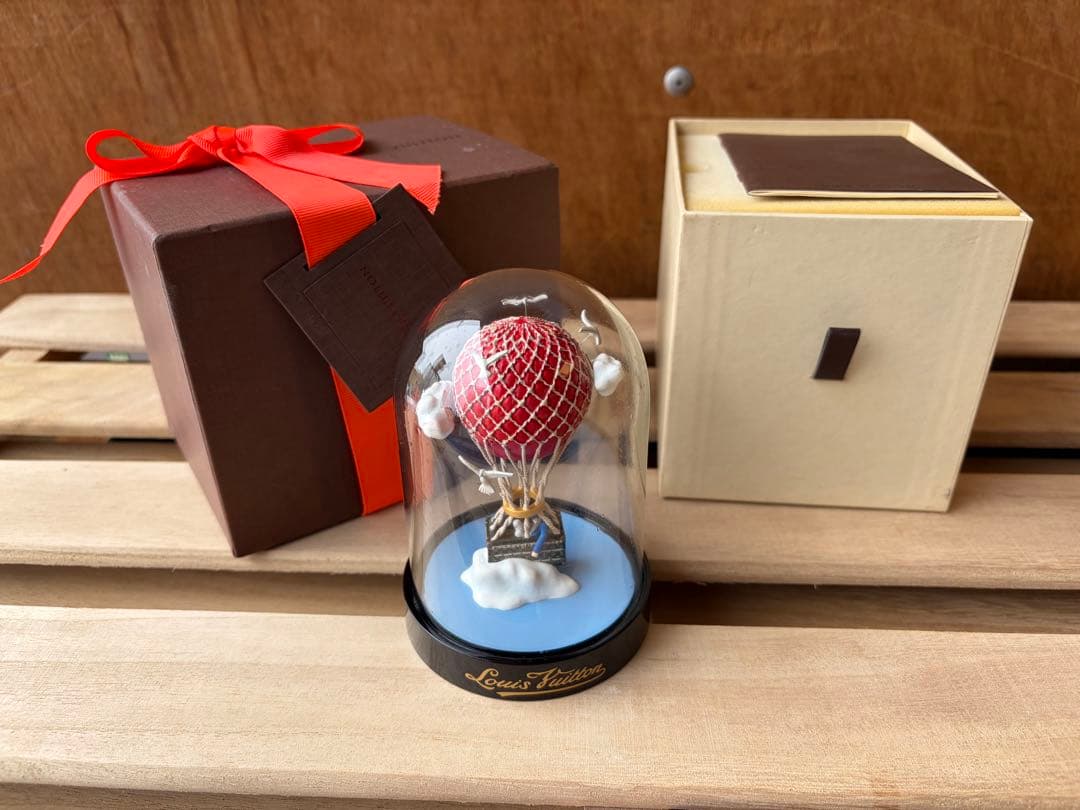 Louis Vuitton miniature hot-air balloon glass ornament displayed under a clear dome with its packaging boxes.