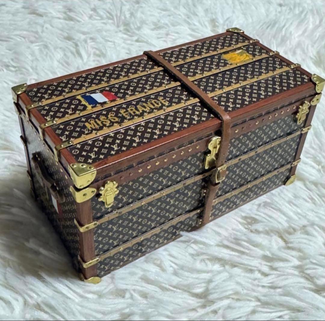Miniature Louis Vuitton monogram trunk paperweight with brass fittings on a fur surface.