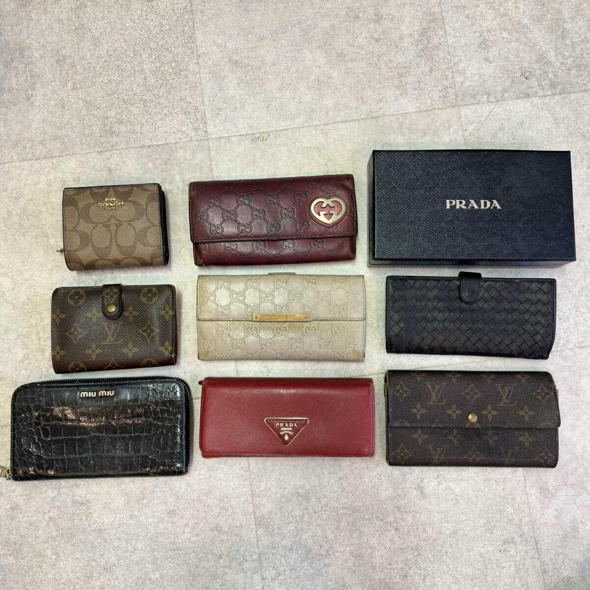 Top-down photo of several leather wallets from brands like Louis Vuitton, Miu Miu, Gucci, Prada, and Coach arranged on a flat tiled surface.