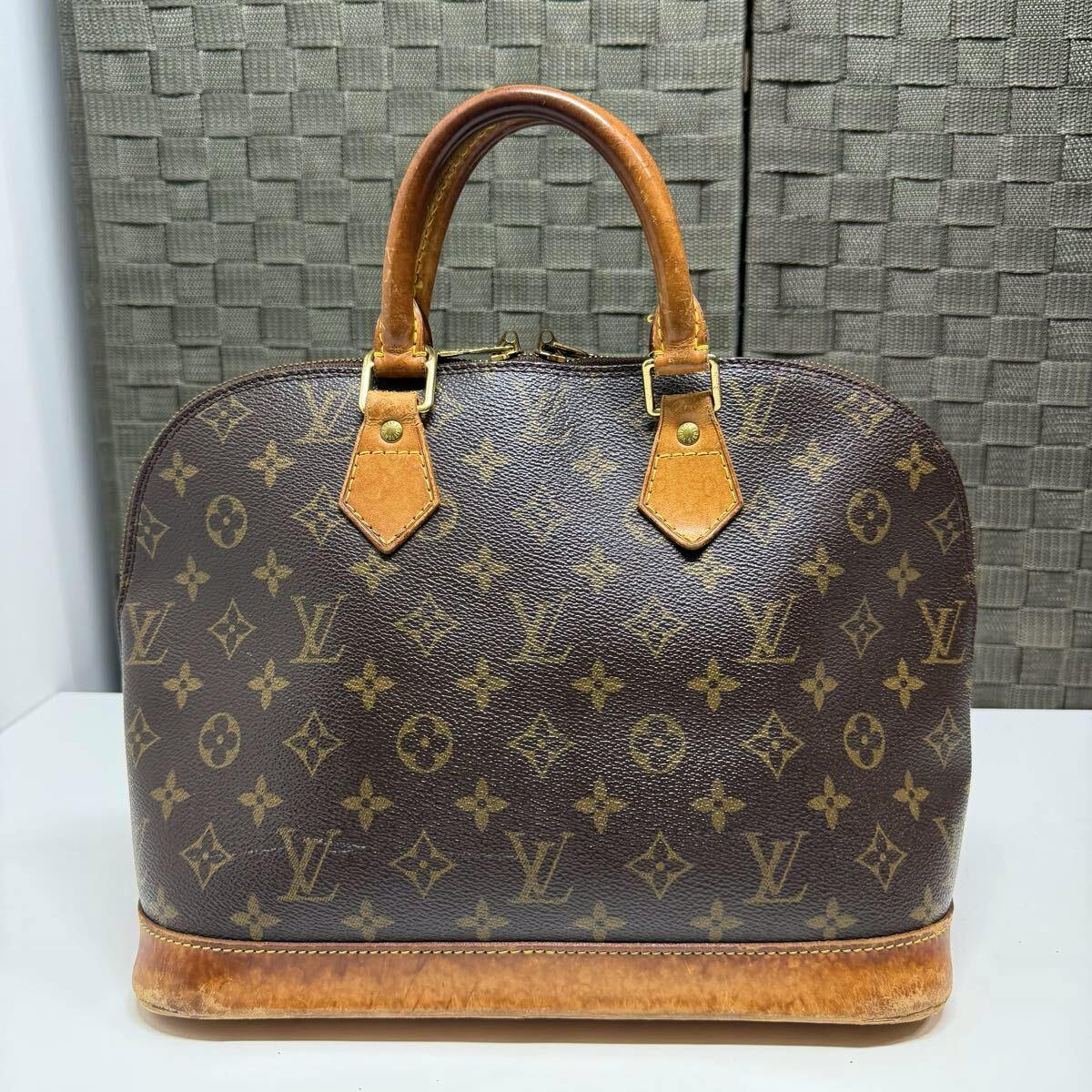 Front view of the brown Louis Vuitton monogram Alma handbag with leather handles.