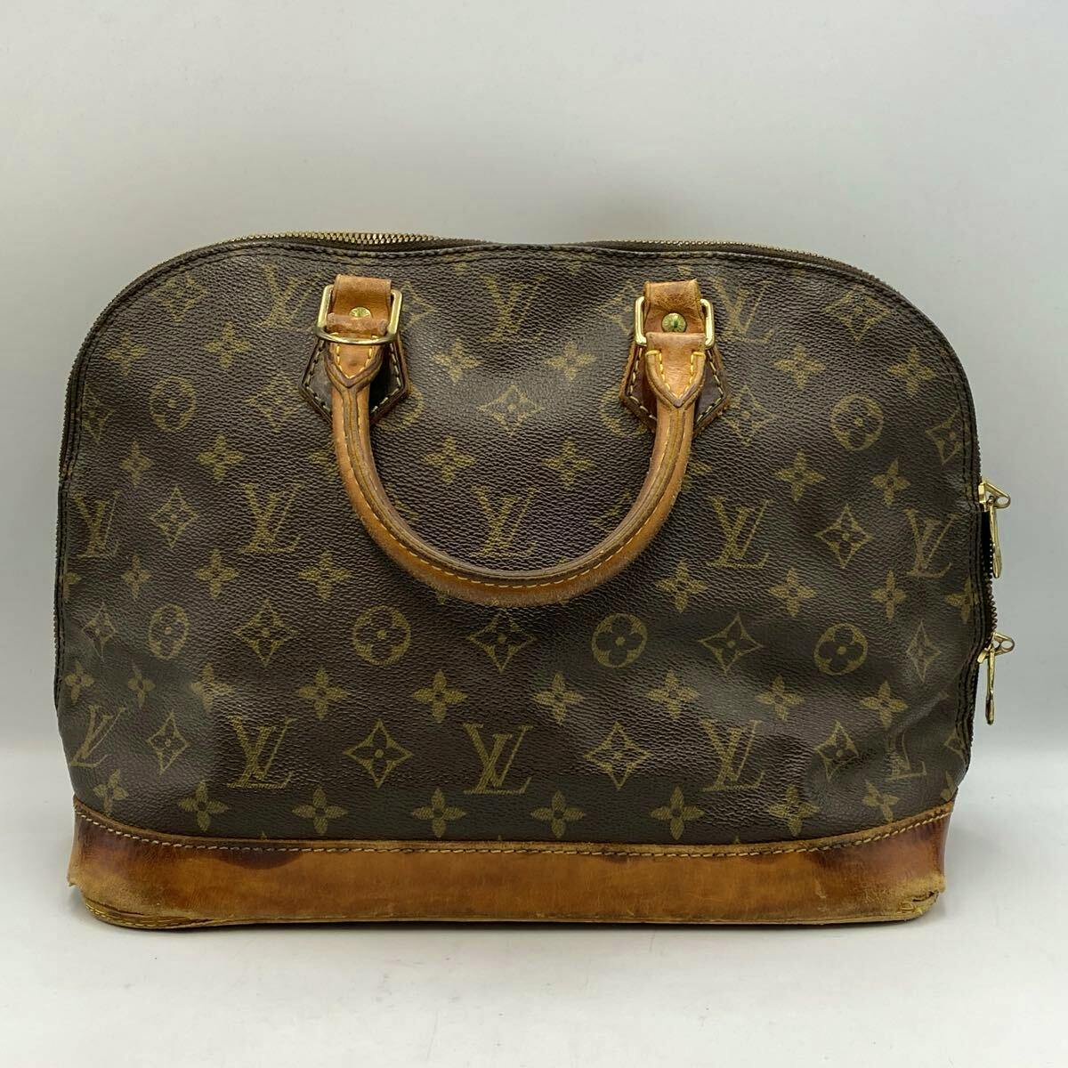 Front view of the Louis Vuitton Monogram Alma handbag with two top handles and a leather base showing wear.