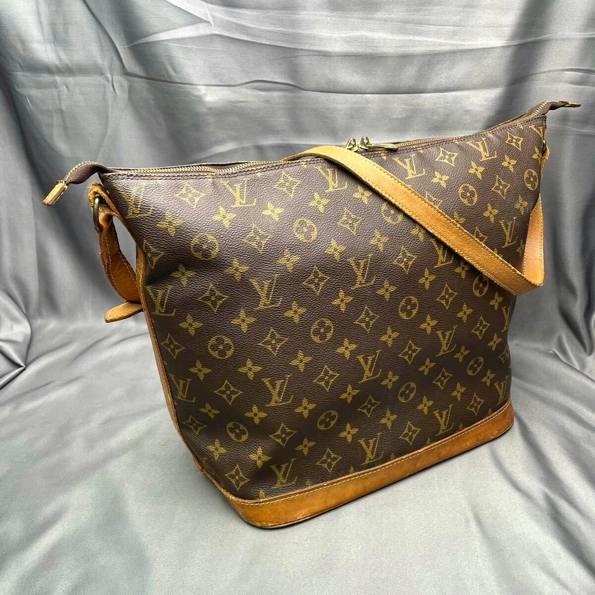 Louis Vuitton monogram shoulder bag with tan leather trim and strap photographed against a gray backdrop.