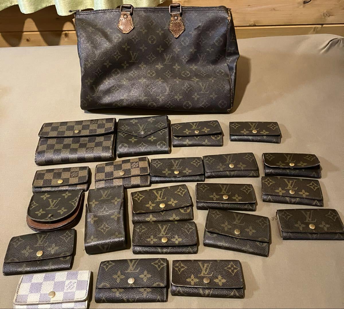 A laid-out assortment of Louis Vuitton monogram and Damier canvas wallets and small leather goods with a monogram tote bag behind them on a flat surface.