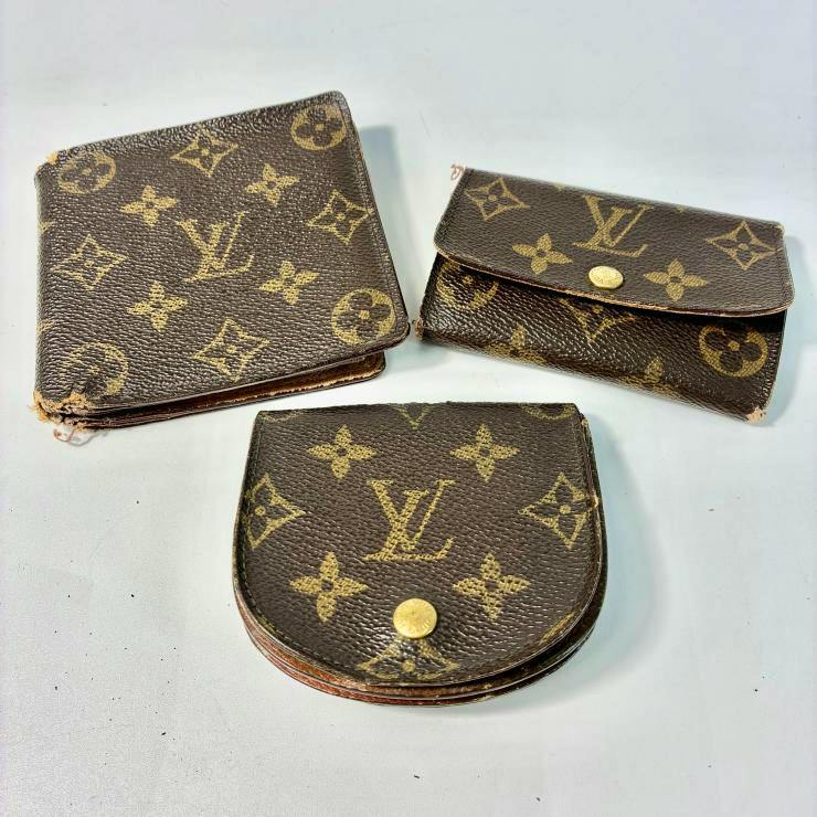 Three Louis Vuitton monogram pieces — a bi-fold wallet, a buttoned coin case, and a flap key case — on a light surface.