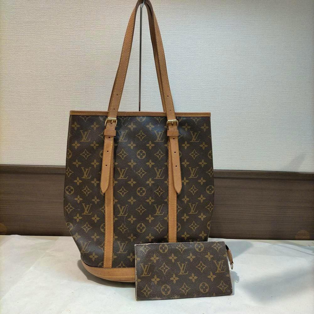 Brown Louis Vuitton monogram handbag with leather straps and a matching pouch placed in front.