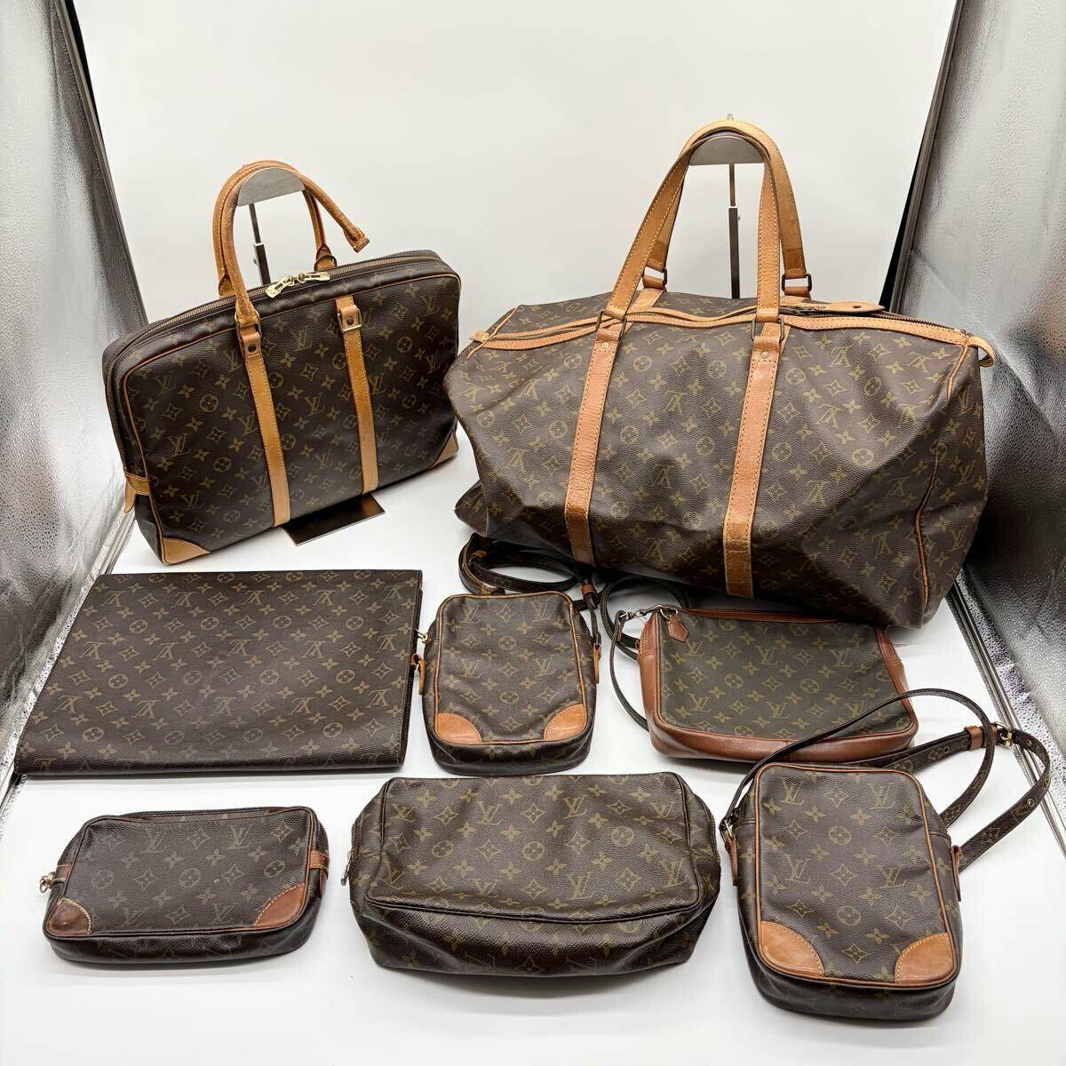 Several Louis Vuitton monogram brown bags and pouches arranged on a white surface, including a large duffel and a briefcase.