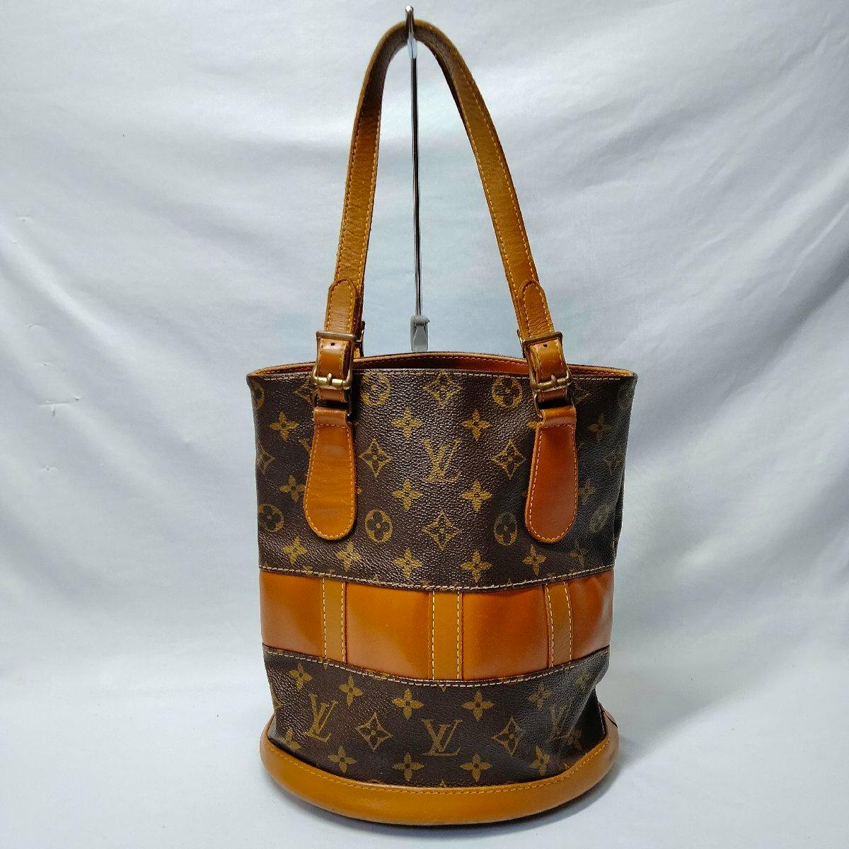 Front view of a Louis Vuitton monogram bucket bag with tan leather trim and shoulder straps on a white background.