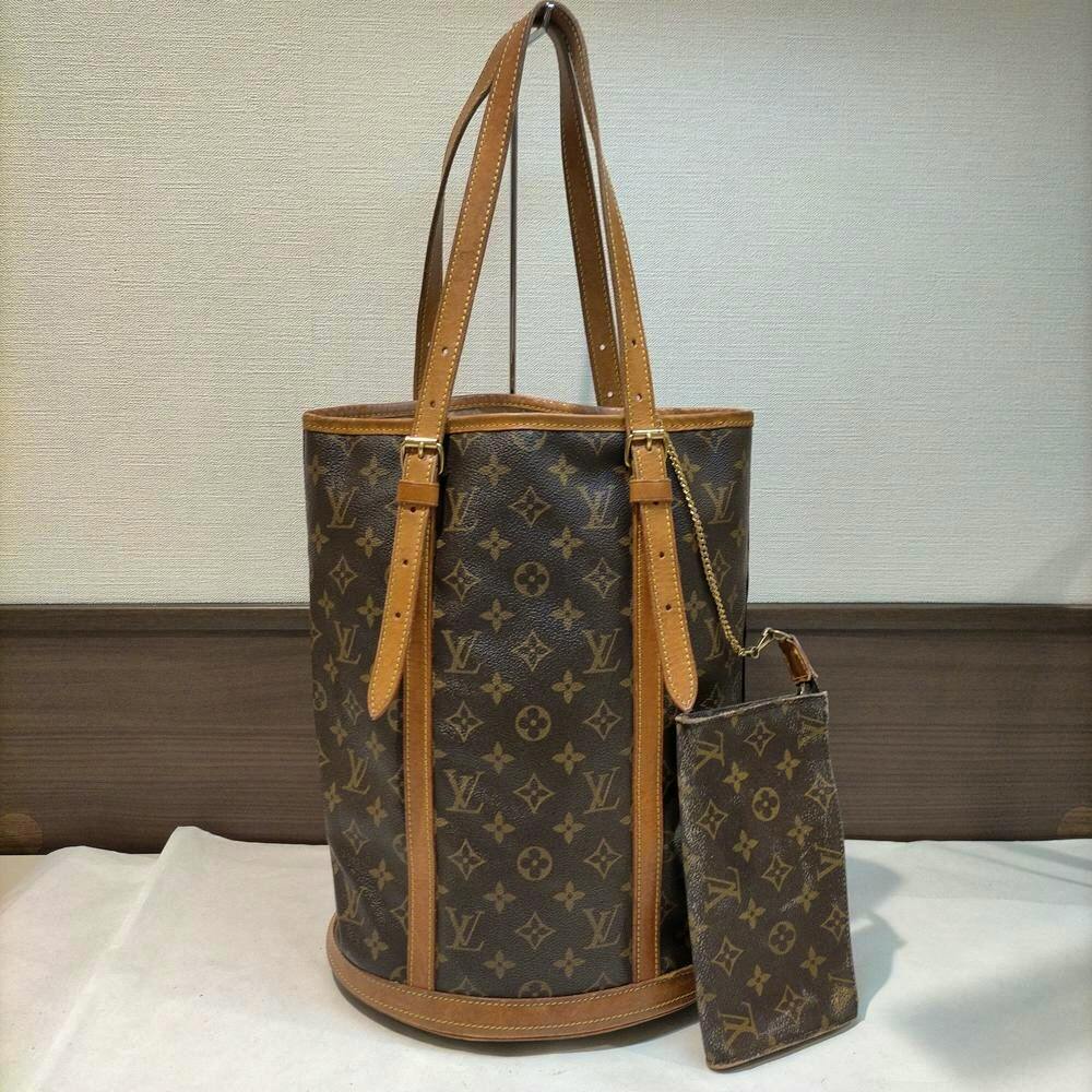 Louis Vuitton monogram bucket bag with leather trim standing upright with a matching pouch attached.