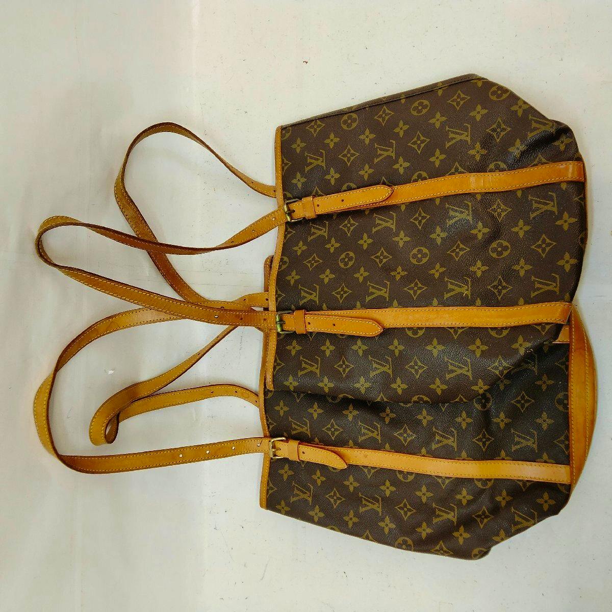 Monogram canvas Louis Vuitton bucket bag with leather straps lying flat on a white surface.