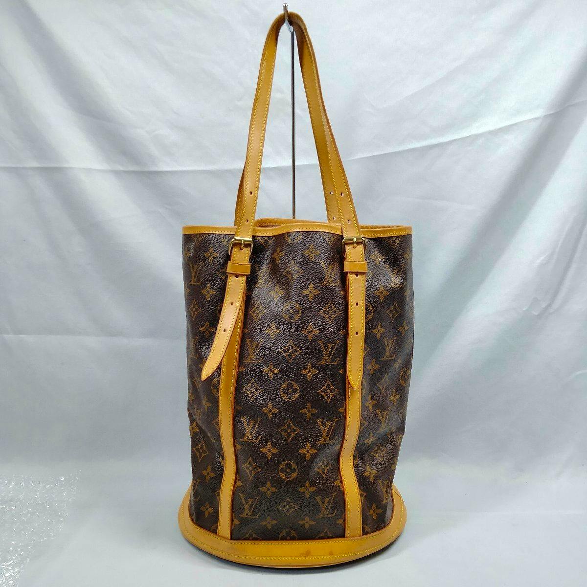 Front view of the Louis Vuitton Monogram Bucket GM bag with cow leather trim and long handles on a plain backdrop.