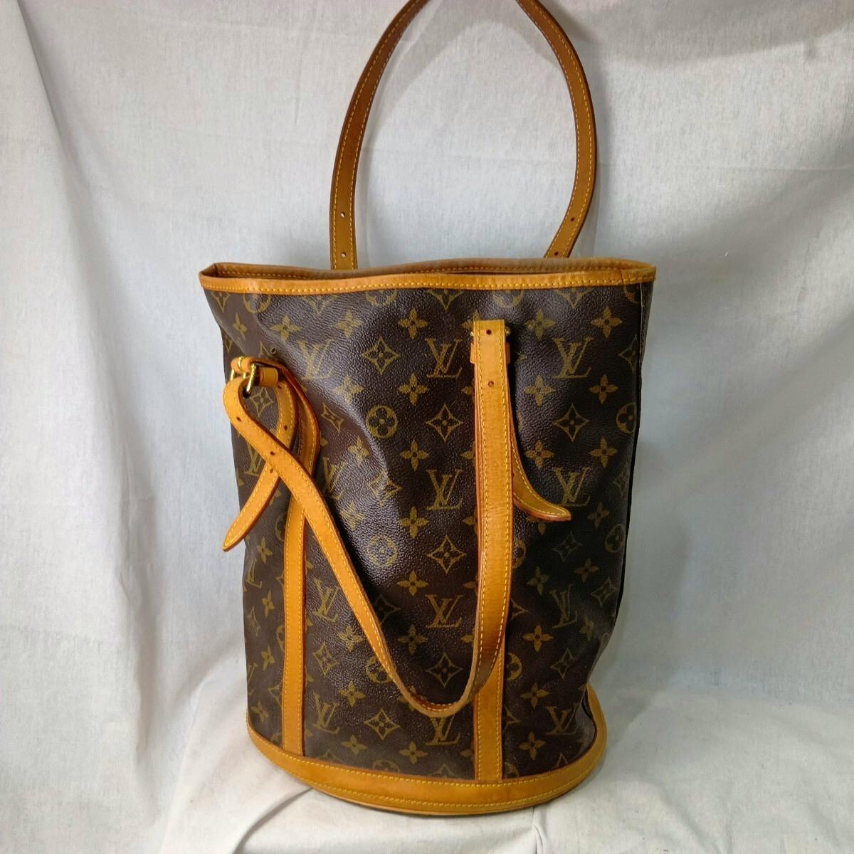 Front view of a Louis Vuitton Monogram Bucket GM canvas tote bag with tan leather trim and shoulder straps against a white background.