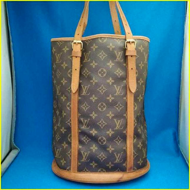 Louis Vuitton monogram canvas Bucket GM bag with leather trim and shoulder straps photographed against a blue background.