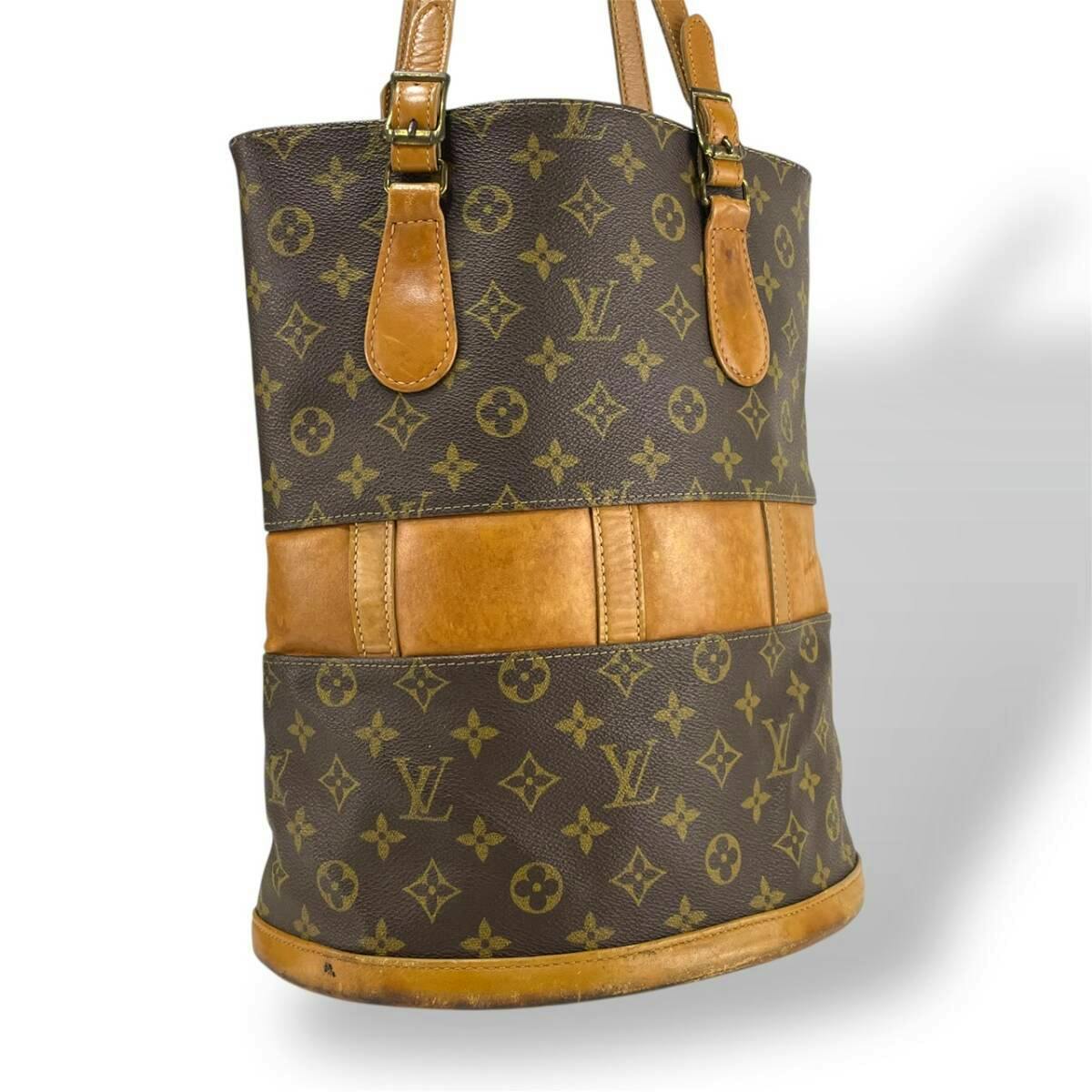 Front view of a Louis Vuitton monogram canvas Bucket GM tote with natural leather trim, base, and shoulder straps visible.