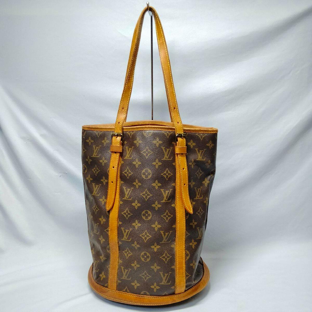 Front view of a Louis Vuitton Monogram Bucket GM tote bag with leather trim and shoulder straps against a plain background.